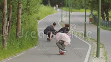 3个年轻人在马路上的绿色公园里玩滑板