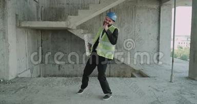 一位建筑工人戴着安全帽，穿着能见度很高的背心，在工地上跳舞很滑稽