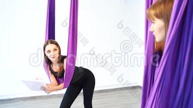 年轻<strong>女子</strong>教练在吊床上练习<strong>瑜伽</strong>前指导一名<strong>女子</strong>。
