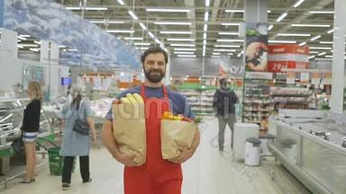 一位身穿红色运动服、手拿购物袋的英俊商店职员站在超市里，他正对着照相机微笑