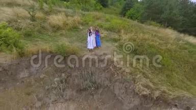 在湖边或河边散步的三个穿着夏日长礼服的女朋友的空中景色。 两个高加索人和一个