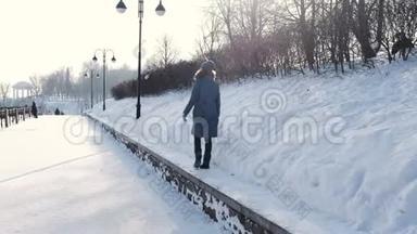 穿着蓝色<strong>羽绒服</strong>的年轻女子在冬季公园沿着边境散步，看着天空，回头看。