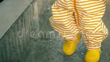 小宝宝穿着橙色条纹防水雨衣和黄色橡胶雨靴在雨后的水坑上散步，特写镜头