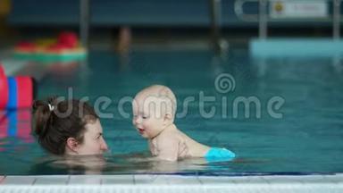 宝宝和妈妈在室内游泳池游泳玩得很开心。 宝贝开心地笑着，他的乳齿清晰可见