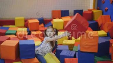 蹦床中心的女孩正在用柔软的多色立方体建造一座城堡。