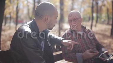 老父亲和成年儿子在公园的长凳上，说话和喝咖啡。 年长父亲的成年儿子教