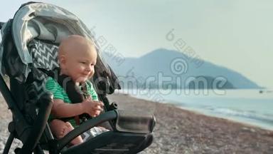 快乐的宝宝在海边的婴儿车里拍手。 小男孩拍手
