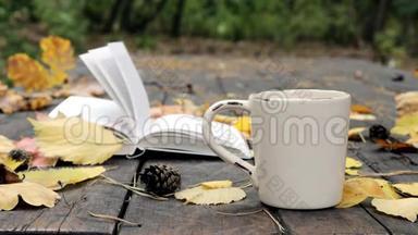 在旧木上躺着一本书，一个杯子里倒着茶、落叶和锥。 风<strong>吹</strong>走了<strong>树叶</strong>，