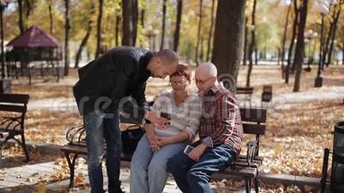 成年儿子在秋季公园的智能手机上显示年迈的父母照片。