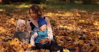 美丽的年轻母亲和两个孩子在树叶上享受<strong>阳光</strong>明媚的<strong>秋日</strong>。