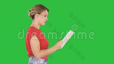 穿着休闲服的女士用数码平板走在绿色屏幕上，按色度键。