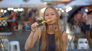 一名年轻女子在亚洲街头市场吃街头食品的慢镜头