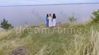 在湖边或河边散步的三个穿着夏日长礼服的女朋友的空中景色。 两名白种人和一名白种人