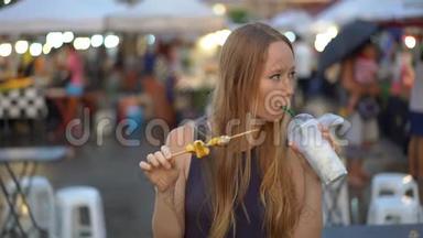 一名年轻女子在亚洲街头市场吃街头食品的慢镜头