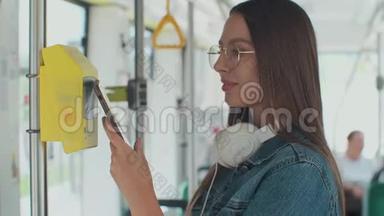 一个年轻微笑的女人在电车上用智能<strong>手机支付</strong>免费的公共交通。