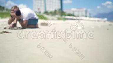 男摄影师拍摄年轻女子在沙滩上摆姿势的照片。 年轻的摄影师