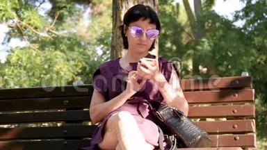 <strong>女孩</strong>坐在公园长凳上，用智能手机在<strong>社交网络</strong>上交流。 年轻的黑发女人