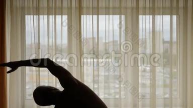 一个男人在室内做运动的剪影。 在背景城市街道的窗帘后面。 男人做热身运动