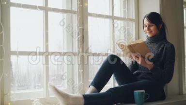 梦中的年轻女子正在阅读书籍，并微笑着坐在窗台上，装饰着照明。 女孩是
