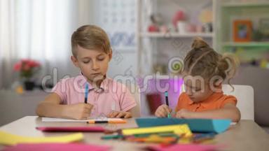 可爱的男孩和女孩坐在桌旁用铅笔画画，幼儿园休闲