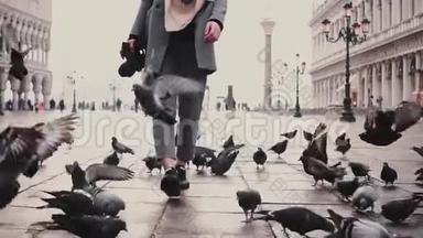 在圣马可广场上，带着一群鸽子在威尼斯慢动作漫步，带着相机散步的美丽女游客快乐