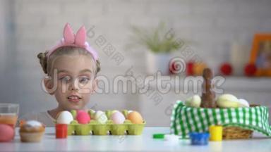 有趣的女孩从桌子底下出现，兴奋地看着染色的复活节彩蛋