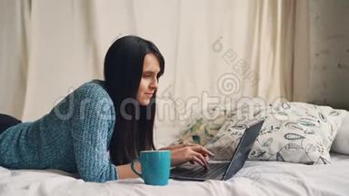 微笑的女士躺<strong>在家</strong>里的床上，用笔记本电脑打字，看着屏幕<strong>上网</strong>。 现代