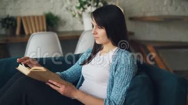 平静的女孩正坐在家里的沙发上看书，翻开书页，享受和平、文学和舒适。 不错的阁楼风格