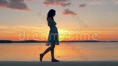 在<strong>夏日</strong>的傍晚，美丽的女人穿着连衣裙沿着海滩漫步在<strong>夕阳</strong>下