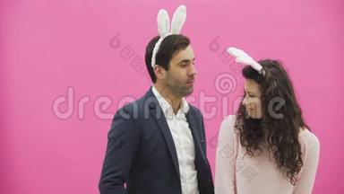 年轻夫妇站在粉红色的背景上。 在此期间，他们进行兔子的运动。 女人把