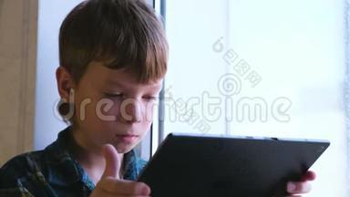 活泼的男孩正坐在窗台上用平板电脑学习科目。