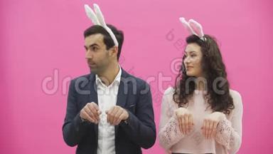 年轻夫妇站在粉红色的背景上。 在这段时间里，他们穿着杂乱的耳朵。 温柔地看着