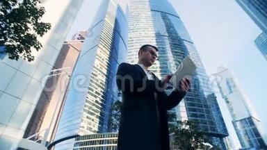 成功的商人正站在摩天大楼旁边操作他的平板电脑。 6K电影院的镜头。