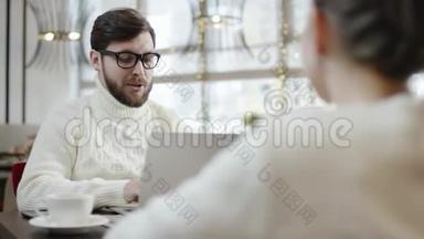 成年男子在咖啡馆的一张桌子旁用笔记本电脑与女友交谈