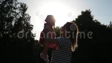 低角度拍摄，年轻可爱的妈妈把她的小女儿抱在怀里，然后在明亮的阳光下拥抱她