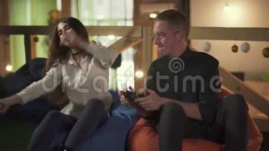 年轻人和女人在咖啡馆里坐在舒适的椅子上玩电子游戏。 可爱的一对夫妇<strong>有约</strong>会，玩得开心