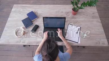 自由职业者女孩在笔记本电脑键盘上输入文字，并在桌旁的剪贴板上写笔记。