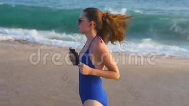 穿着泳衣在海边跑步和听音乐的年轻女子。 女孩沿着海边慢跑。 女<strong>运动</strong>员