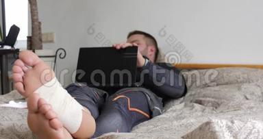 一个腿受伤的蓄胡子男人用笔记本电脑完成任务，开始在卧室里思考