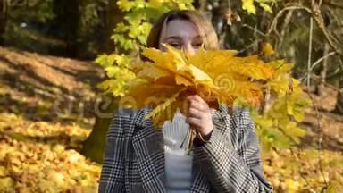 可爱的年轻、开朗、快乐的女孩把脸藏在秋天公园的一片黄色枫叶后面