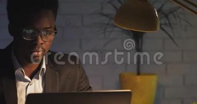 疲惫的年轻商人<strong>深夜</strong>在他的笔记本电脑上辛勤<strong>工作</strong>。 睡懒觉的人坐在黑暗的办公室里的办公桌前。 他推迟了
