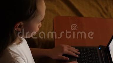 笔记本电脑上搜索引擎中的女孩打字查询。 孩子们晚上在房间里玩电脑。 年轻女孩在做家庭作业