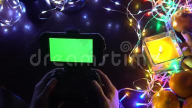 手动使用带有智能手机色度键绿色屏幕的游戏垫。 以蜡烛、花环、彩灯组成圣诞新年，