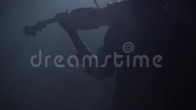 在<strong>黑</strong>暗的工作室里的女孩拉小提琴，从一个灯笼眩光围绕着房间。 <strong>黑烟</strong>背景。 背面