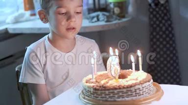 男孩坐在厨房的桌子上，在生日蛋糕上吹蜡烛，许愿
