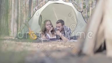 <strong>肖像</strong>年轻男子漂亮的年轻女子躺在森林里的帐篷里，在<strong>看书</strong>。 木块