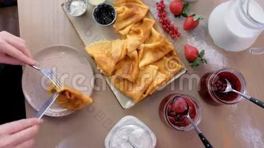 女人正在吃俄罗斯传统的薄煎饼，在盘子里放上果酱、酸奶油和草莓。 特写