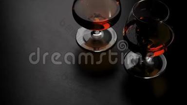 豪华白兰地。 两杯金色干邑酒在黑桌上旋转。 玻璃在灯光下眩光。 白兰地，白兰地，嗅探器，狂欢。