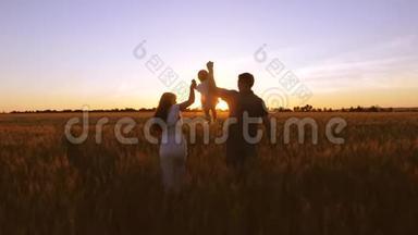 爸爸妈妈把快乐的孩子抱起来，宝宝笑了。 一个快乐的家庭孩子，爸爸妈妈带着小麦在田里散步