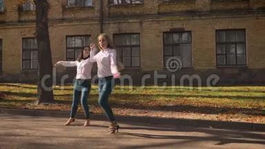 在阳光明媚的日子里，两个很棒的白人女孩在街上跳舞，被鼓舞，快乐，展示